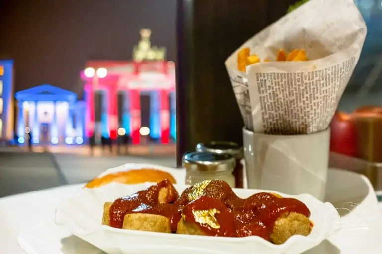 Goldene Currywurst in Berlin essen mit Blick auf das Brandenburger Tor